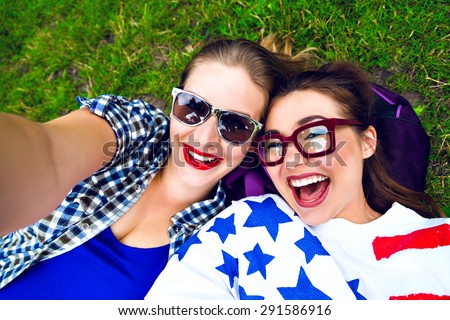 Two hipster girls having fun and making selfie in the park, smiling and screaming, wearing sunglasses and bright clothes, best friends relax end enjoy weekend.