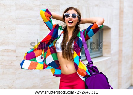 Bright summer trendy portrait of young fit girl walking on the street, wearing vivid shirt crop top and leg gins holding big sportive bag, long hairs and make up, smiling, screaming, joy.