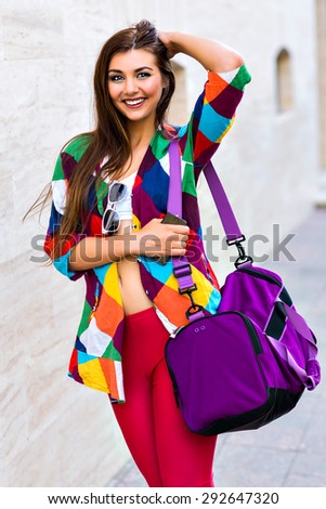Bright summer trendy portrait of young fit girl walking on the street, wearing vivid shirt crop top and leg gins holding big sportive bag, long hairs and make up.