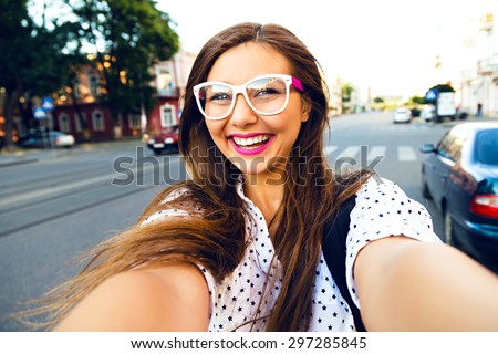 Young smiling teen happy woman making selfie on the street, ling hairs, bright make up and cute clear glasses, traveling alone, having fun, positive mood, joy, vacation.