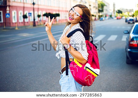 Summer city portrait of stylish teen girt, traveling alone with backpack, having nice day in new town, enjoy her vacation, wearing backpack, hipster glasses and casual look, joy, emotions.
