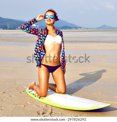 Outdoor lifestyle portrait of surfer girl posing at California beach, have perfect sportive tanned body, having active time at lonely exotic island, bright outfit, sunny colors.