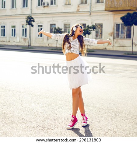 Outdoor summer lifestyle image of young pretty hipster woman having fun, listening music and dancing on the street, city center Europe, cute white vintage outfit and sunglasses, fun ,joy, emotions.