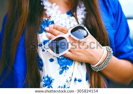 Fashion details, floral dress. stylish jewelry, woman holding sunglasses on her hand, toned colors, street style.