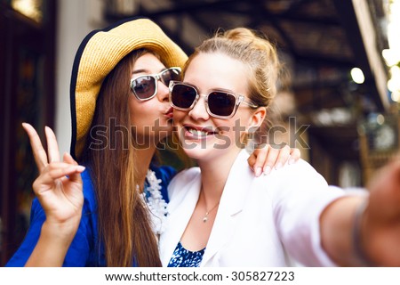 Cute pretty girls making funny selfie on the street, kissing to the cheek, having fun together,  joy, positive, love, friendship, sisters.