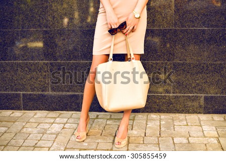 Outdoor fashion details, sexy woman wearing elegant beige clothes and hight heels, stylish classic accessorizes, toned colors.