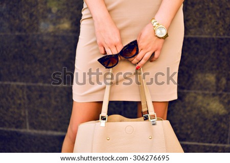 Close up fashion details, young business woman holding bag and retro sunglasses, golden jewelry, warm colors.