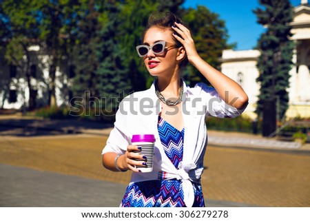 Stylish sexy girl traveling at Europe, drinking tasty latte, enjoy her trip, wearing bright printed summer romper, trendy jewelry and vintage sparkled sunglasses, bright toned colors.