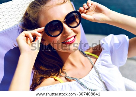 Cute smiling girl laying on the beach, traveling and enjoy her summer vacation, posing near pool, perfect skin, trendy sunglasses and jewelry, toned colors.