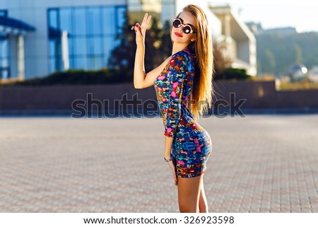 Sunny positive portrait of sexy stunning girl in short bight dress jumping and having fun on the street, joy, happiness, weekends, bright colors.