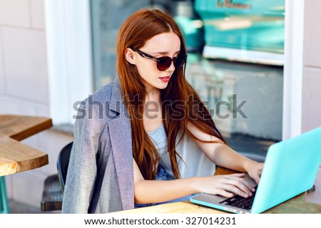 Outdoor city fashion portrait of young businesswoman working at cafe on terrace at sunny day, casual stylish outfit, mint details, using her laptop, cafe break, business concept.