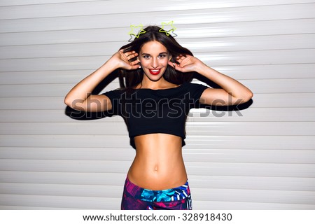 Young sexy sportive woman,going crazy and having fun at with urban background, bright clothes and make up, crop top, printed pants, raspy for party.