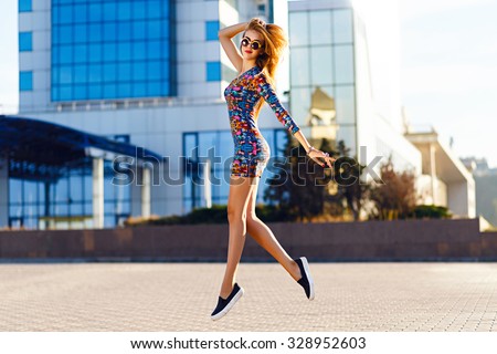 Happy positive summer portrait of cute sexy woman in bright mini dress jumping on the street, sunny day, urban style, make up, fashion accessorizes .
