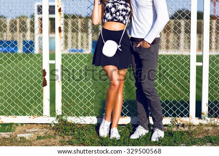 Fashion details, young hipster couple posing at sports ground, wearing trendy hipster black and white casual clothes and sneakers, sunny day , bright colors.
