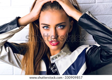 Close up fashion studio portrait of stunning brunette woman with big blue eyes, full sexy lips and perfect skin, bright glamour make up, wearing biker leather jacket.