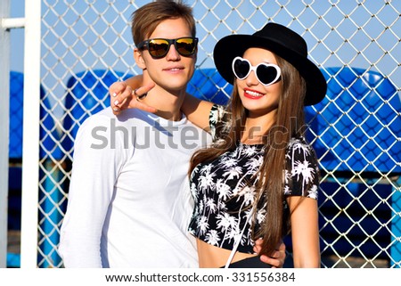 Outdoor fashion portrait of hipster couple in love hugs at sport ground, trendy black and white clothes, vintage sunglasses, posing at romantic date, sunny day, bright colors, love, relations.