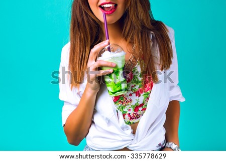 Close up studio portrait of sexy hipster woman with full lips, wearing bright outfit, holding and drinking tasty green smoothie milkshake , sweet pastel colors, ming blue background.