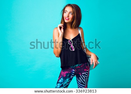 Studio fashion portrait of sexy hipster woman, tanned perfect skiing bright make up, trendy sportive outfit, printed leggings, silver backpack, student party look, mint blue background.