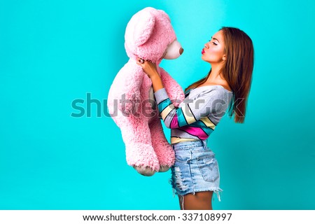 Studio funny portrait of pretty  woman playing with big fluffy teddy bear, mint background, sweet pastel colors. holding her present and sending kiss, making funny face, holidays, joy, childhood.