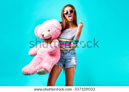 Young hipster woman playing with big fluffy pink toy bear, showing tongue and middle finger, wearing sexy mini shorts and sunglasses, cheeky emotions, yo, cool, crazy.