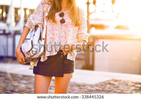 Outdoor fashion image of woman wearing mini leather skirt, cozy relaxed light sweater , silver backpack, vintage sunglasses, fashion close up details, sunshine autumn colors.