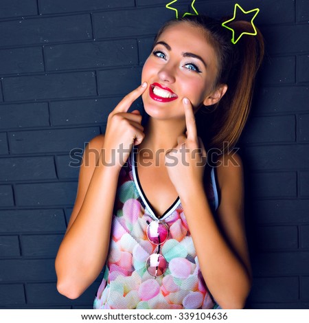Indoor funny crazy portrait of pretty hipster girl wearing trendy bright clothes accessorizes and make up, black brick urban wall, amazing big smile, positive mood, happy time.