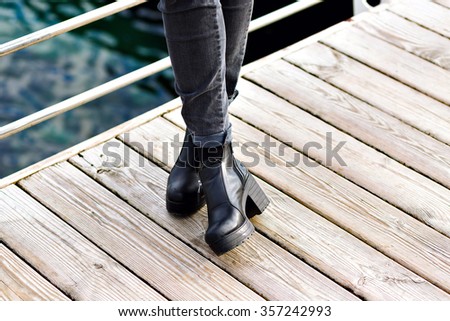 Close up fashion image of retro brutal boots, woman posing at wooden floor near sea, street style, total black, hipster look.
