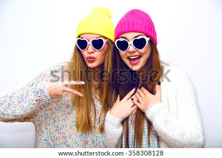 Trendy hipster portrait of young funny girls, hugs and having fun, going crazy together, party winter holiday time, neon sweaters hats vintage hearted sunglasses, emotions, joy, swag, flash.