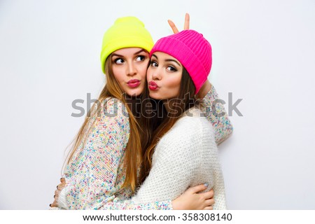 Cute positive portrait of best friend pretty young girls, winter time, neon hats, cozy sweaters, hugs and having fun, natural glowing makeup, two sisters sending air kiss, joy, couple, emotions.