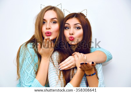 Indoor fashion lifestyle portrait of pretty teen happy friends girls, hugs, wearing cozy pastel cashmere mint sweaters, brunette and blonde hairs, make up, trendy accessory, sending air kiss.