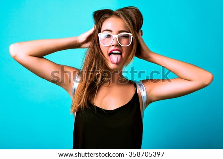 Studio bright crazy portrait of cheeky young woman screaming showing tongue and winking, blue background, black top, cheerful funny style, sportive tanned body, party fun.