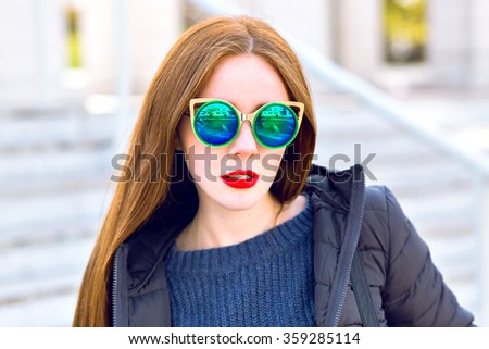 Close up outdoor fashion city portrait of young woman, amazing long ginger hairs, trendy mirrored blue sunglasses, coat and sweater, cold spring sunny time, bright colors.