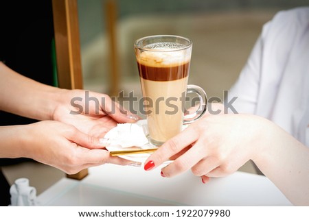 Closeup of woman\'s hands taking the latte cup from hands of a barista in a coffee shop