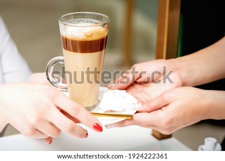 Closeup of woman's hands taking the latte cup from hands of a barista in a coffee shop