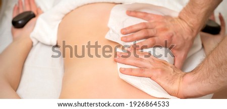 Hands of a masseur with towel massaging back of a young adult woman in spa salon