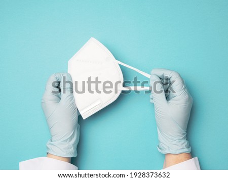hand hold white disposable medical mask on a blue background, personal protective equipment for the respiratory tract from viral infections, top view