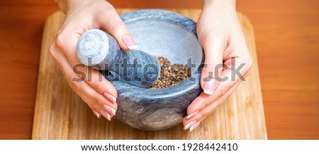 Female hands grind dry pepper spices in mortar on a wooden kitchen board