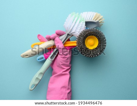 female hand in a pink glove holds a stack of plastic cleaning brushes, blue background
