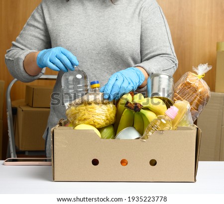 woman in gloves keeps collecting food, fruits and things and a cardboard box for helping those in need, the concept of help and volunteering. Delivery of products