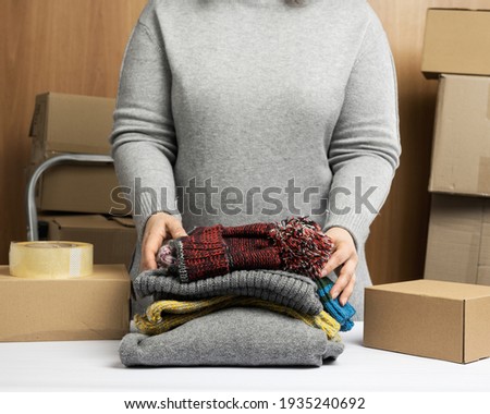 woman in a gray sweater collects clothes in a box, concept of assistance and volunteering, moving. Selling unnecessary things