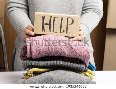 woman in a gray sweater collects clothes in a box, concept of assistance and volunteering