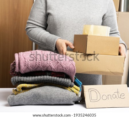 woman in a gray sweater is packing clothes in a box, the concept of assistance and volunteering, close up