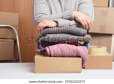 woman in a gray sweater is packing clothes in a box, the concept of assistance and volunteering, moving. Selling unnecessary things