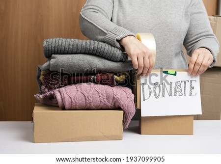 woman in a gray sweater is packing clothes in a box, the concept of assistance and volunteering, donation