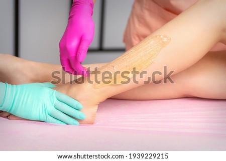 Two female cosmetologists waxing woman\'s legs with hot sugar paste in a beauty spa salon