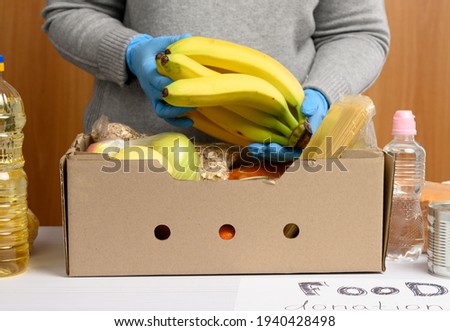 woman in gloves keeps collecting food, fruits and things and a cardboard box for helping those in need, the concept of help and volunteering