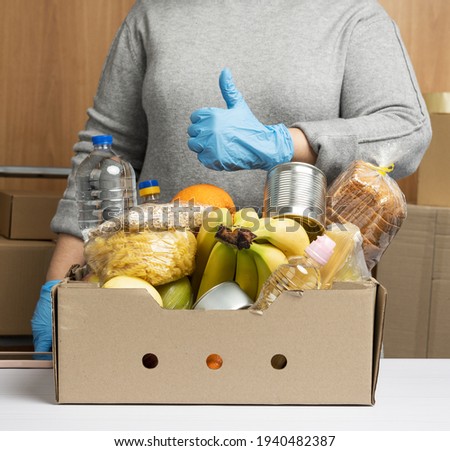 woman in gloves keeps collecting food, fruits and things and a cardboard box for helping those in need, the concept of help and volunteering. Delivery of products