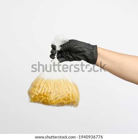 female hand in a black glove holds a transparent bag with raw fusilli pasta on a white background