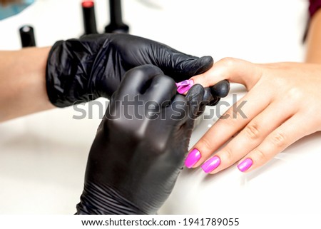 Close up of manicure master applying pink nail polish to female nail in a nail salon