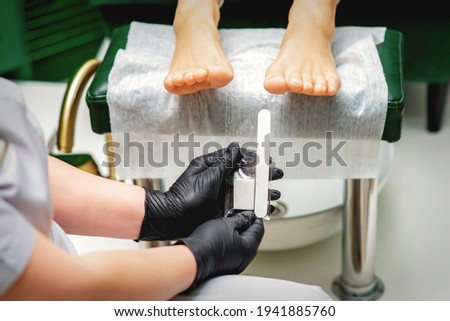 Nail file tool in hands of chiropodist before procedure files nails on toes in a nail salon